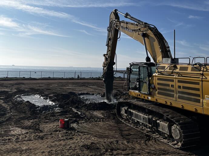 excavator with attachment performing soil mixing on beach front property